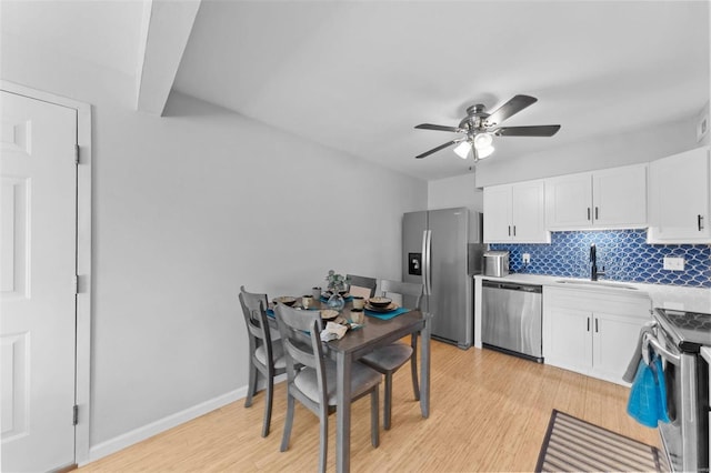 kitchen featuring tasteful backsplash, light wood finished floors, appliances with stainless steel finishes, white cabinets, and a sink