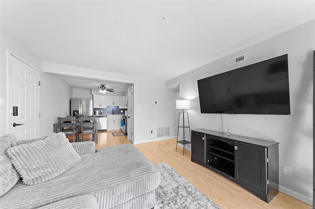 living room with visible vents, baseboards, light wood-style floors, and ceiling fan