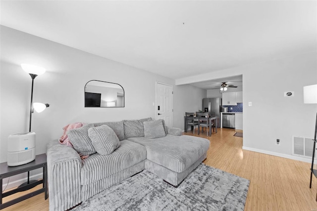 living room with visible vents, light wood-style flooring, a ceiling fan, and baseboards