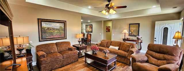 living area featuring baseboards, a ceiling fan, a raised ceiling, and wood finished floors