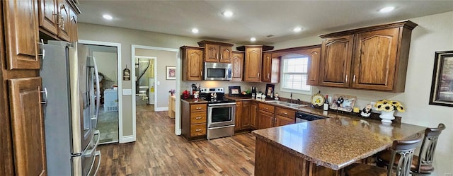 kitchen featuring dark countertops, appliances with stainless steel finishes, dark wood-style flooring, a peninsula, and a sink