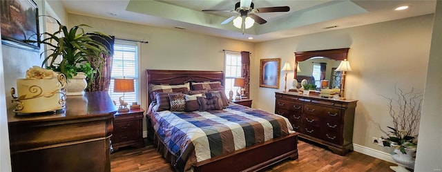 bedroom featuring a tray ceiling, multiple windows, and dark wood finished floors