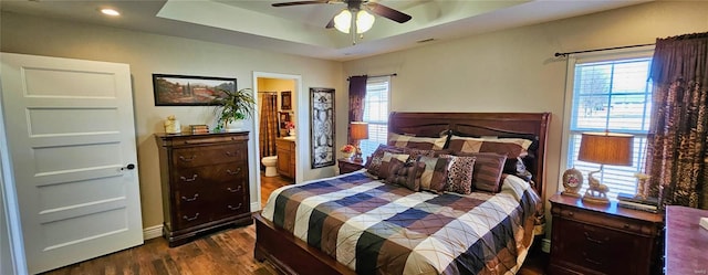 bedroom with baseboards, multiple windows, a tray ceiling, and dark wood-style flooring