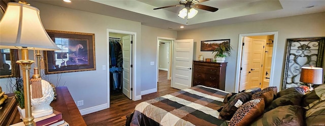 bedroom featuring a walk in closet, a closet, a raised ceiling, wood finished floors, and baseboards