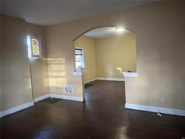 unfurnished room featuring plenty of natural light, arched walkways, and baseboards