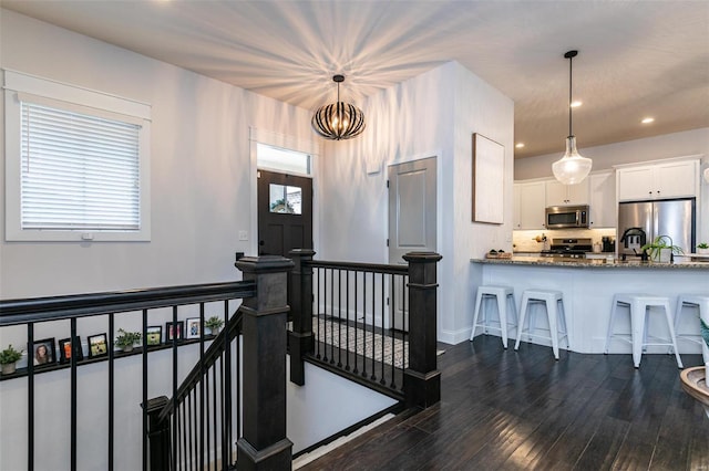 interior space with stone countertops, dark wood-style floors, appliances with stainless steel finishes, a kitchen breakfast bar, and white cabinetry