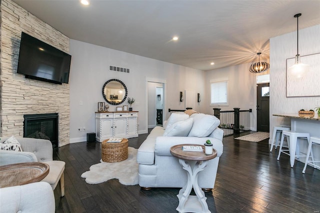 living area with baseboards, visible vents, hardwood / wood-style floors, a stone fireplace, and recessed lighting