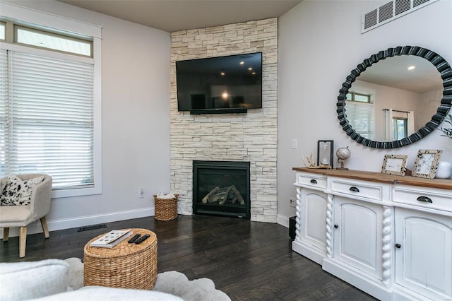 living room featuring baseboards, a fireplace, visible vents, and dark wood-type flooring