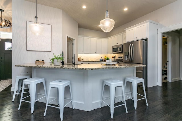 kitchen with light stone counters, dark wood-style flooring, a breakfast bar area, appliances with stainless steel finishes, and white cabinetry