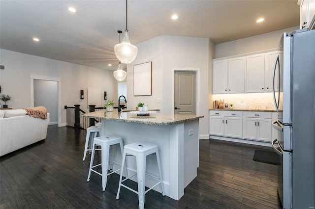 kitchen with dark wood-style floors, freestanding refrigerator, white cabinets, and light stone countertops