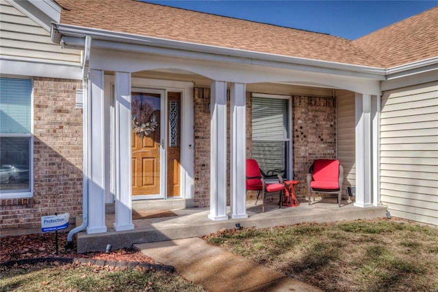 doorway to property with a shingled roof, brick siding, and a porch