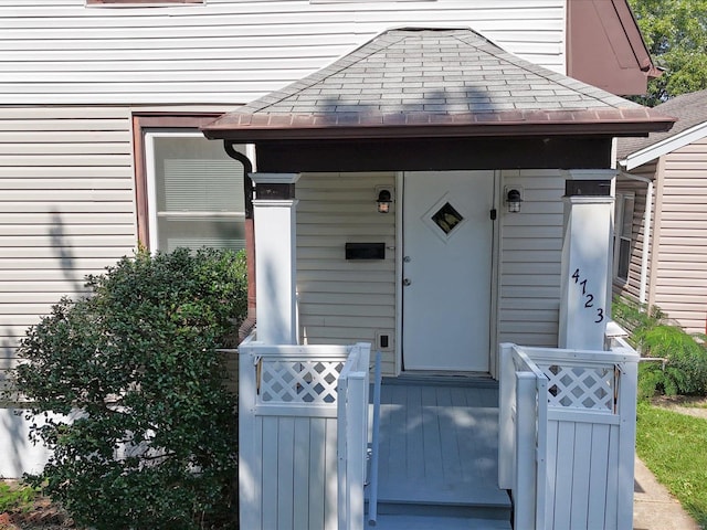 doorway to property with a shingled roof, a porch, and fence