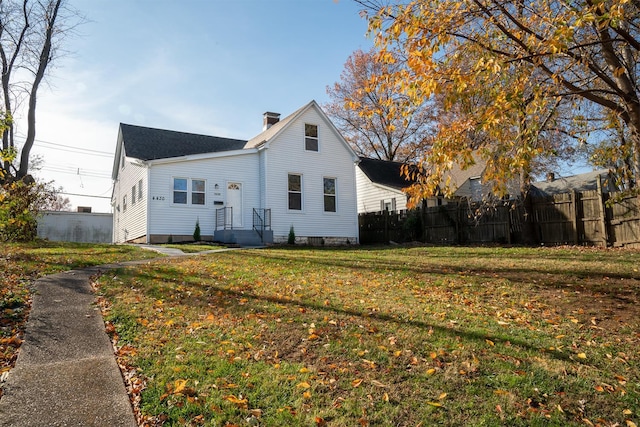 view of front of house featuring a chimney, fence, and a front lawn