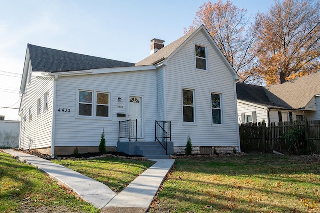 view of front of house with a chimney, roof with shingles, a front yard, and fence