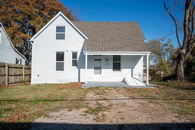 view of front of house with covered porch, fence, a front lawn, and roof with shingles