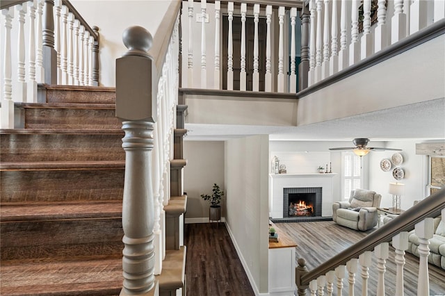 stairs featuring baseboards, a fireplace, a high ceiling, wood finished floors, and a ceiling fan