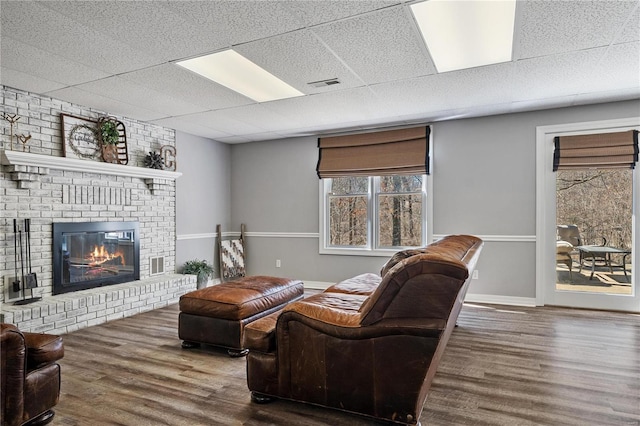 living area featuring visible vents, wood finished floors, a paneled ceiling, baseboards, and a brick fireplace