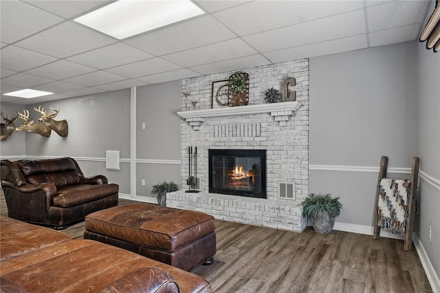 living room with visible vents, a drop ceiling, wood finished floors, baseboards, and a brick fireplace