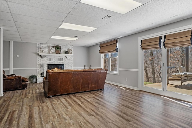 living room with visible vents, a brick fireplace, a paneled ceiling, and wood finished floors