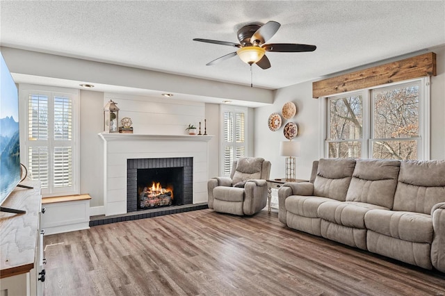 living room with a textured ceiling, a brick fireplace, wood finished floors, and a ceiling fan