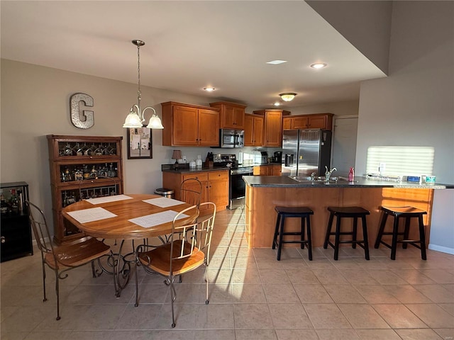 kitchen featuring brown cabinets, stainless steel appliances, dark countertops, a sink, and a kitchen breakfast bar