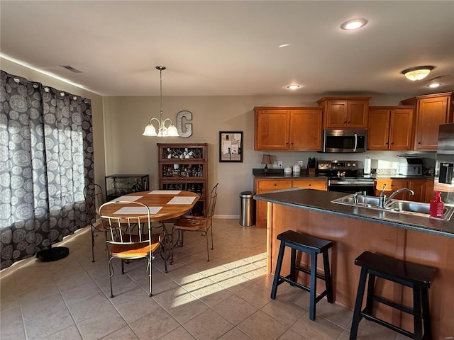 kitchen with stainless steel appliances, a sink, brown cabinetry, dark countertops, and a kitchen bar