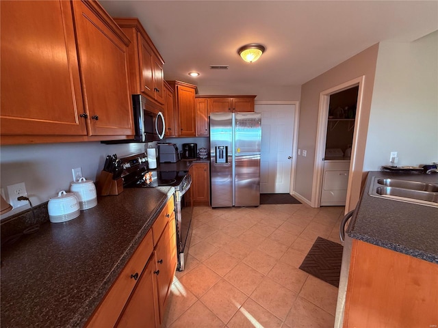 kitchen featuring light tile patterned flooring, stainless steel appliances, a sink, visible vents, and brown cabinetry