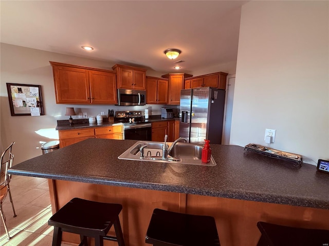 kitchen featuring a breakfast bar, dark countertops, appliances with stainless steel finishes, brown cabinetry, and a sink