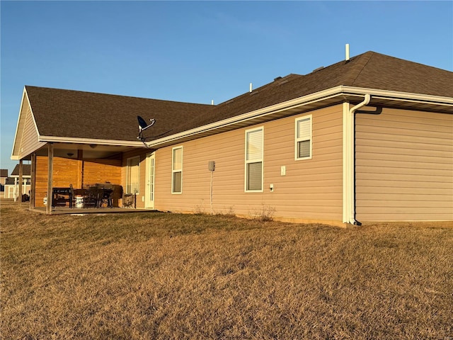 rear view of house featuring a patio, a lawn, and roof with shingles