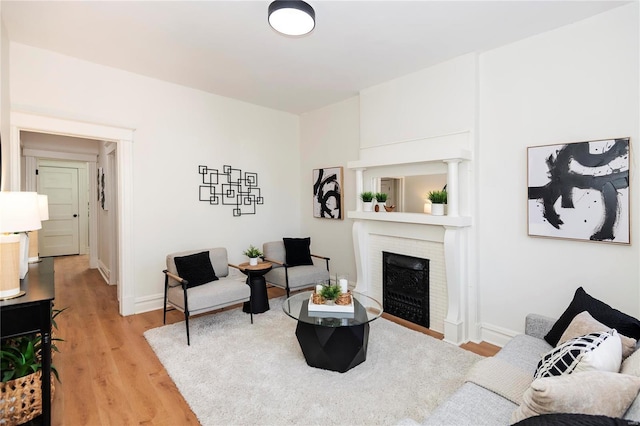 living room featuring a brick fireplace, light wood-style floors, and baseboards