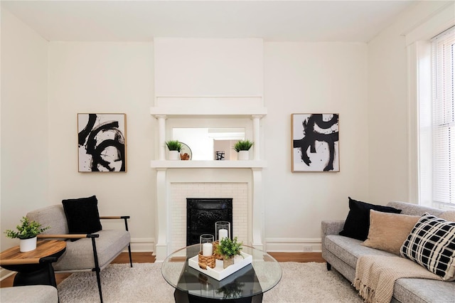 living area featuring a brick fireplace, baseboards, and wood finished floors