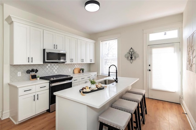 kitchen with a kitchen bar, a sink, stainless steel microwave, gas range oven, and white cabinetry