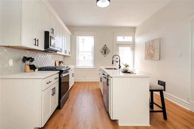 kitchen with a sink, light wood-style floors, appliances with stainless steel finishes, a kitchen breakfast bar, and tasteful backsplash