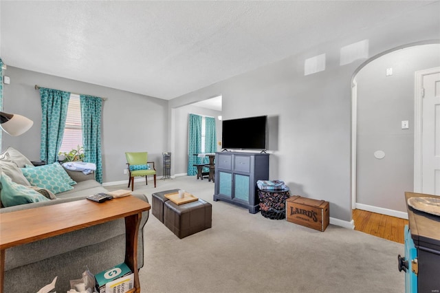 carpeted living area featuring baseboards, arched walkways, and a textured ceiling