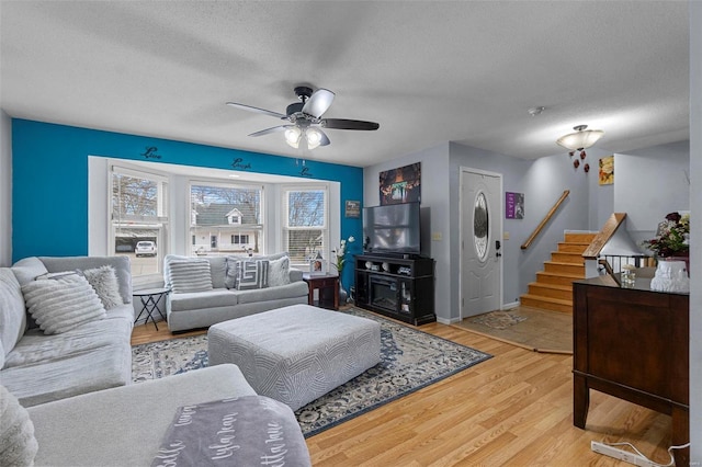 living room featuring light wood-style floors, ceiling fan, stairway, and a textured ceiling