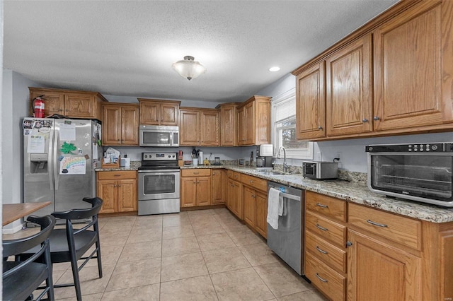 kitchen featuring appliances with stainless steel finishes, brown cabinets, a sink, and light tile patterned flooring