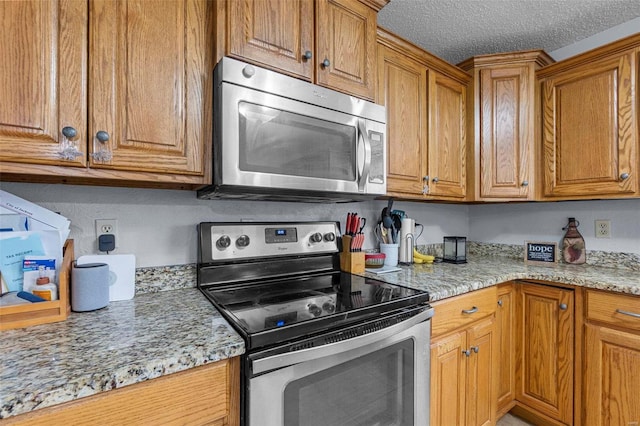 kitchen featuring light stone counters, appliances with stainless steel finishes, brown cabinetry, and a textured ceiling