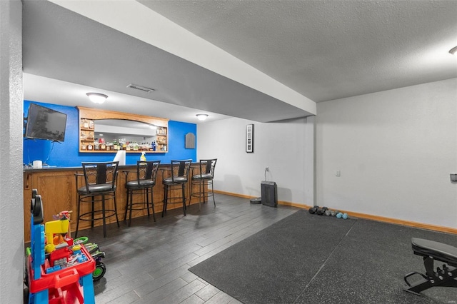 recreation room with a dry bar, visible vents, a textured ceiling, wood finished floors, and baseboards