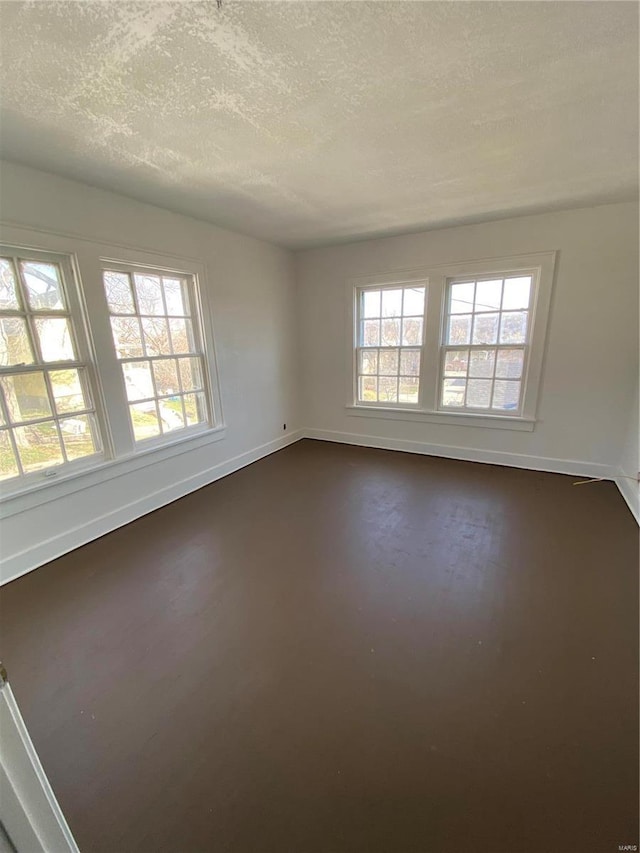 unfurnished room with concrete floors, baseboards, and a textured ceiling