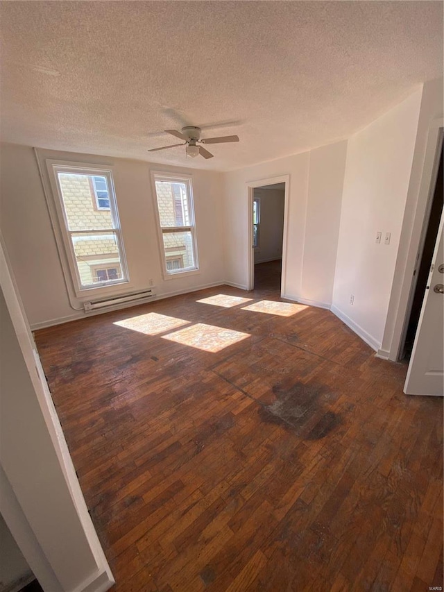 empty room featuring dark wood finished floors, a baseboard heating unit, ceiling fan, a textured ceiling, and baseboards