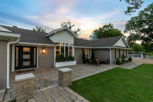 back of property at dusk featuring brick siding, a yard, a shingled roof, a patio area, and fence