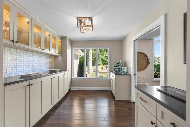 kitchen with tasteful backsplash, white cabinets, dark countertops, glass insert cabinets, and dark wood-type flooring