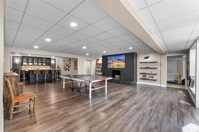 playroom with wood finished floors, a brick fireplace, bar area, and a paneled ceiling