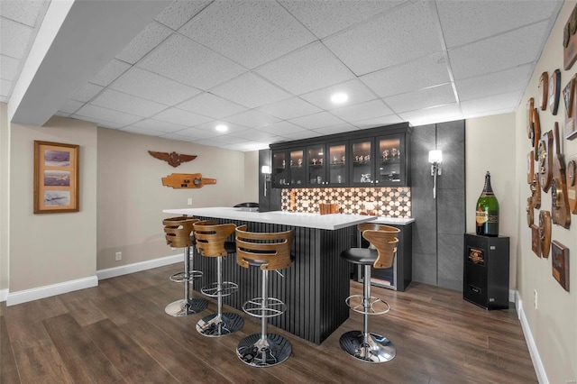 bar featuring a paneled ceiling, wet bar, baseboards, and dark wood finished floors