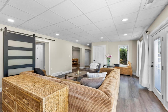 living room with a barn door, dark wood finished floors, and baseboards