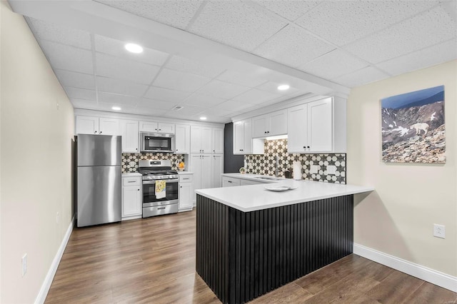 kitchen with tasteful backsplash, light countertops, appliances with stainless steel finishes, white cabinets, and a peninsula