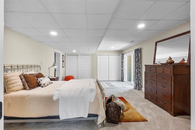 bedroom with recessed lighting, light carpet, a paneled ceiling, and two closets