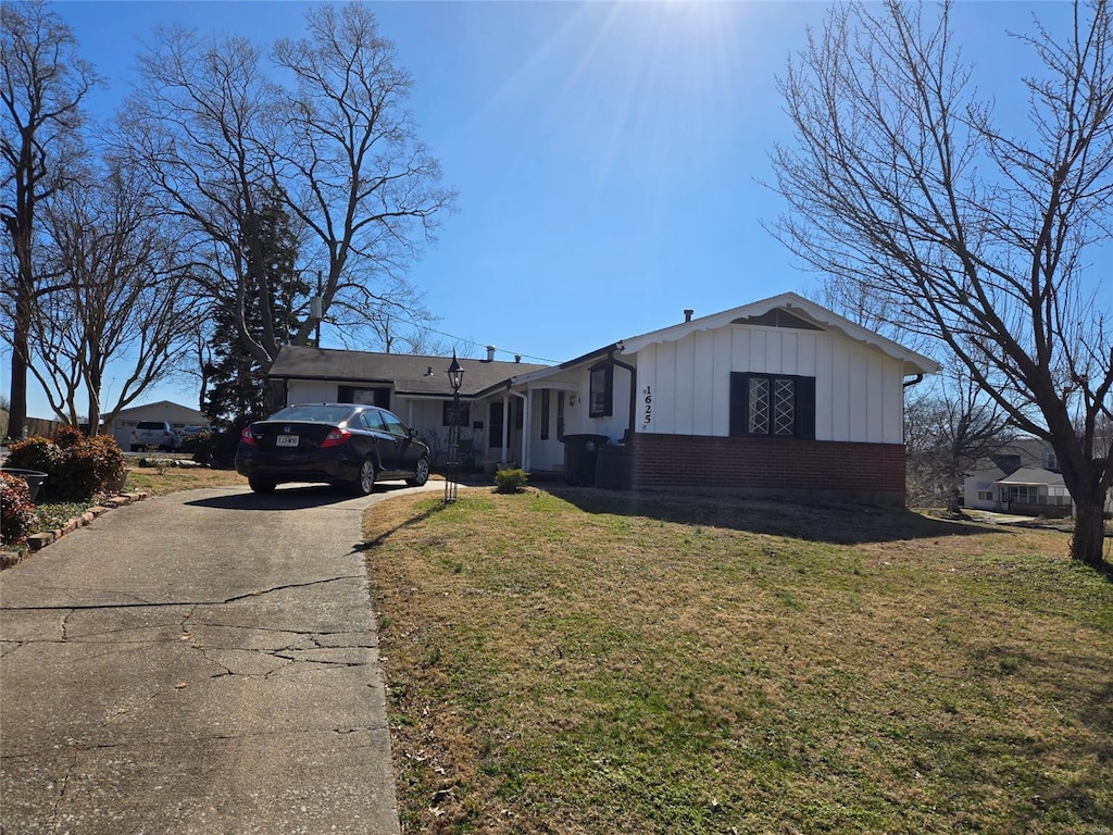 ranch-style house featuring board and batten siding, a front yard, brick siding, and driveway