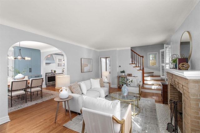 living room featuring light wood-style flooring, arched walkways, an inviting chandelier, a fireplace, and stairs