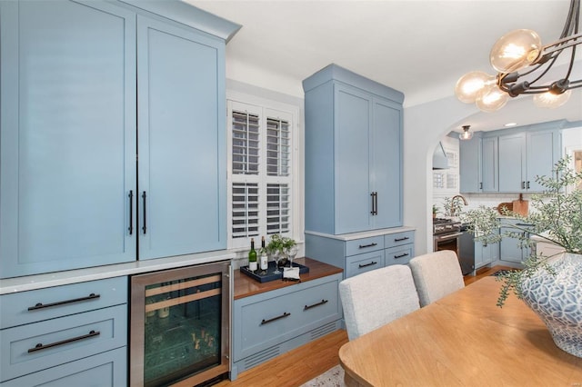 kitchen featuring arched walkways, stainless steel stove, wine cooler, light wood-style floors, and a notable chandelier